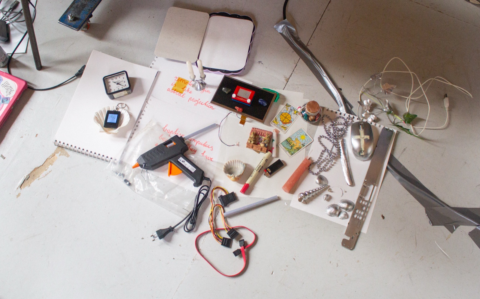cyberbirdxx's studio floor: tarot cards, shells, a glue gun, sata cables, a silver mouse and handwritten notes reading "remote is like astral projection"