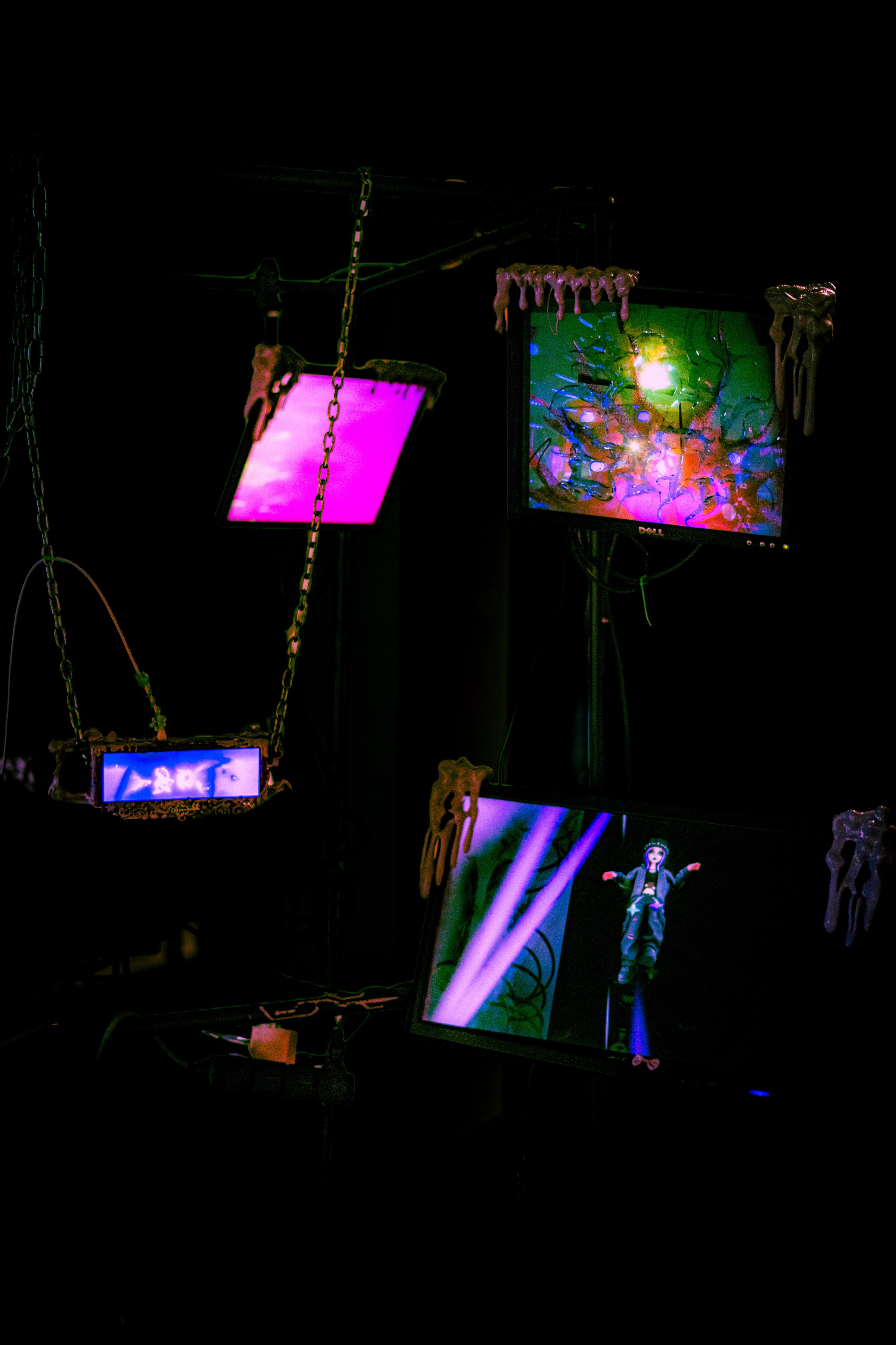 the rig lit low: a dell panel dripping thick beige slime over a green and magenta smeared image, a bright pink blank panel beside it, a lower screen with the arms-spread avatar walking a violet corridor, a slime-framed panel on chain at left