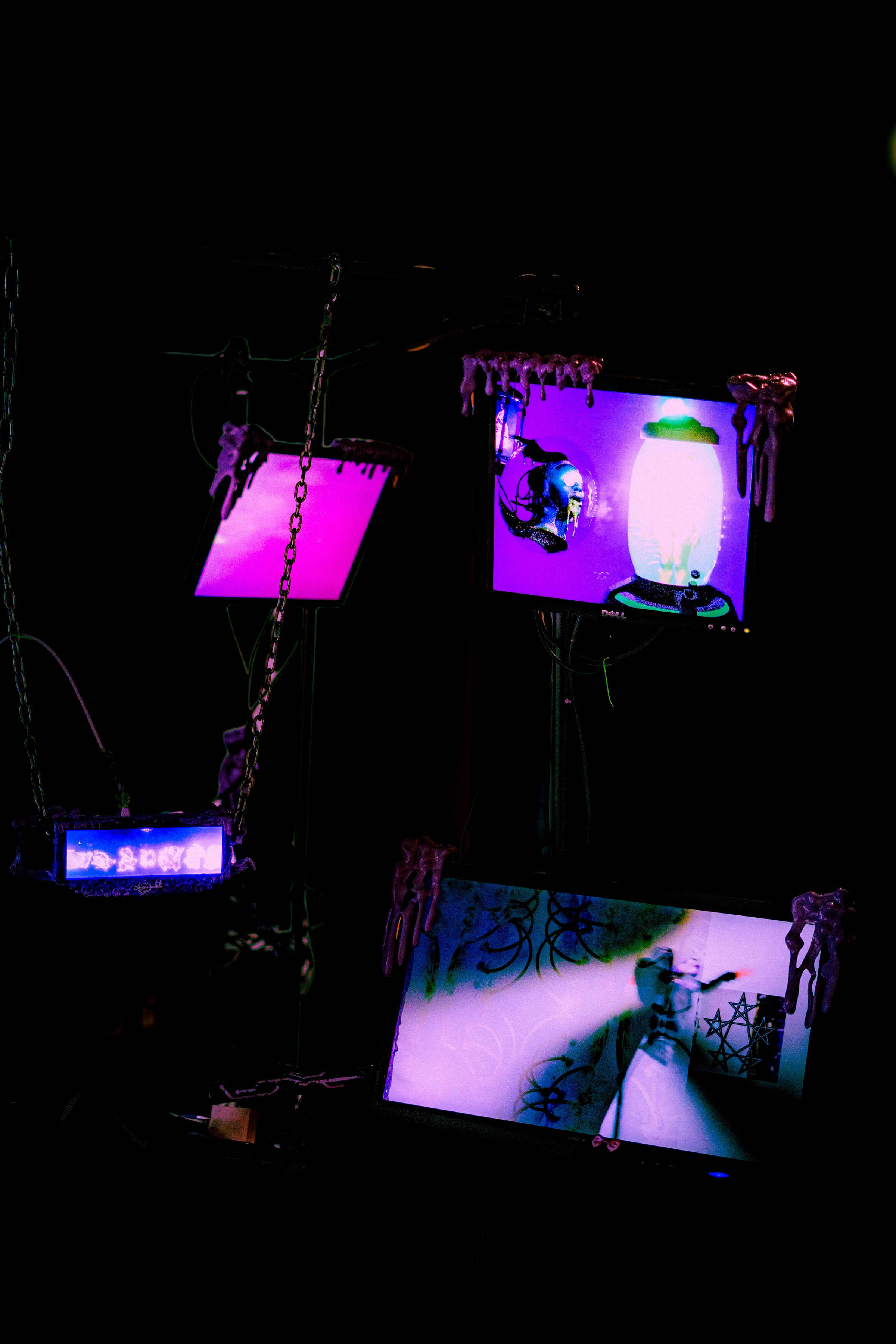 the rig from the front, slime hands over every bezel, an upper screen showing a chrome figure beside a glowing white urn, a lower screen showing a robed white figure with a pentagram diagram, a bright pink panel and a chained water panel to the left