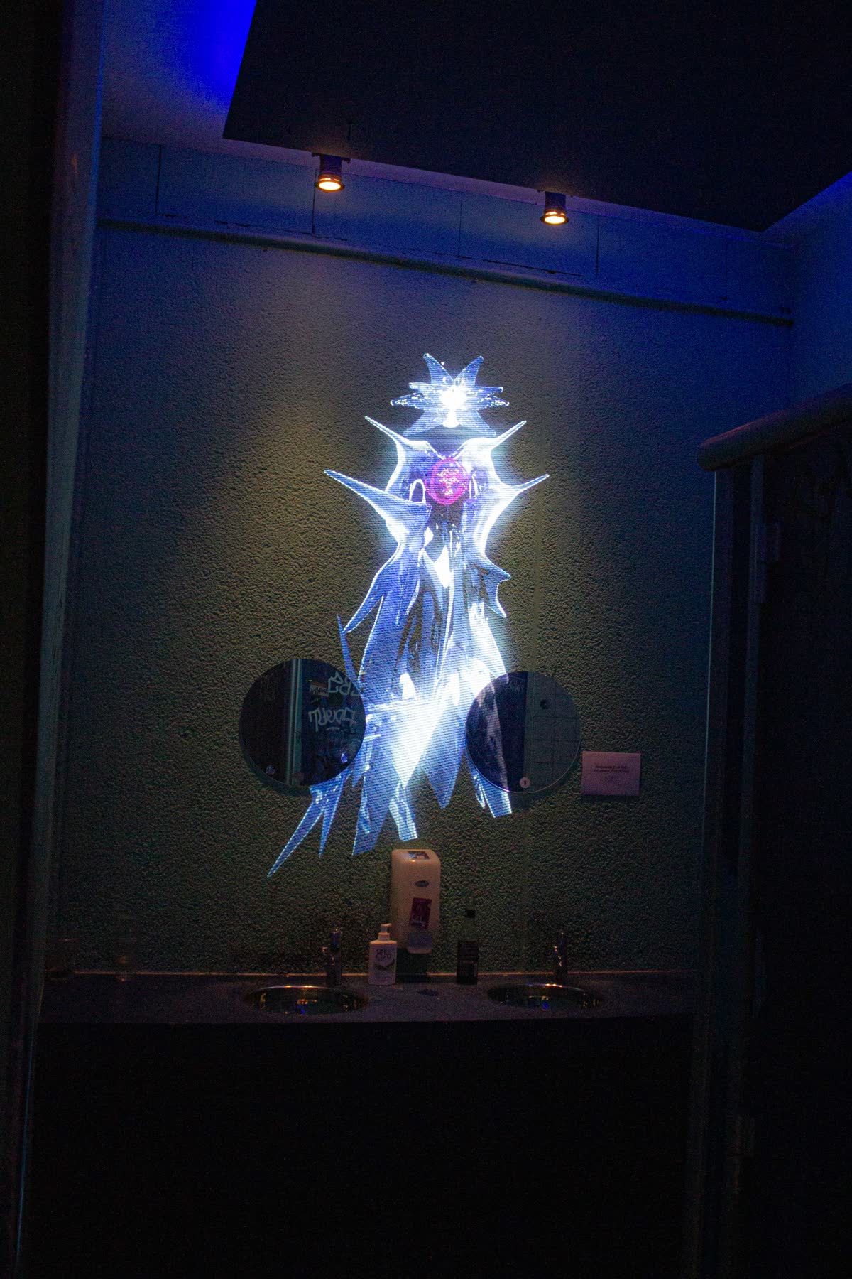the spined, crowned figure projected in cold blue and white, the ceiling lamps burning orange above it