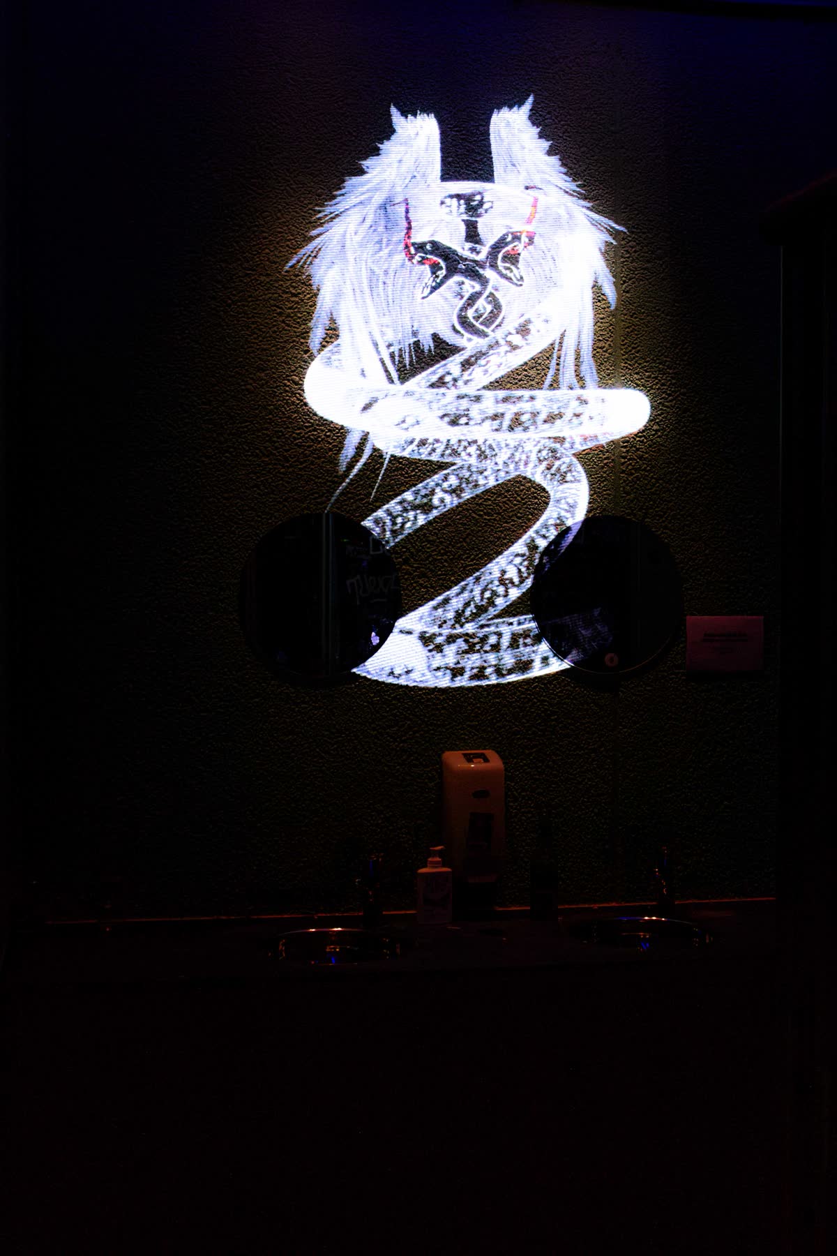 the room gone almost entirely black, only the white winged figure and its coiled ribbon burning on the wall