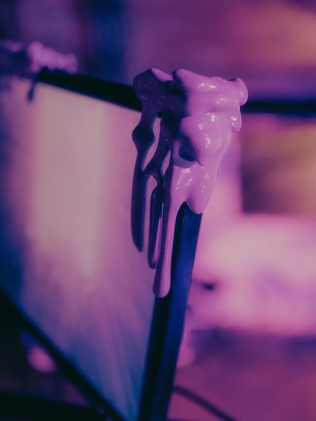 close up of thick pale cyberslime poured over a black bar and the corner of a monitor, hardened into hanging drips with rounded tips. a lit screen glows out of focus behind.