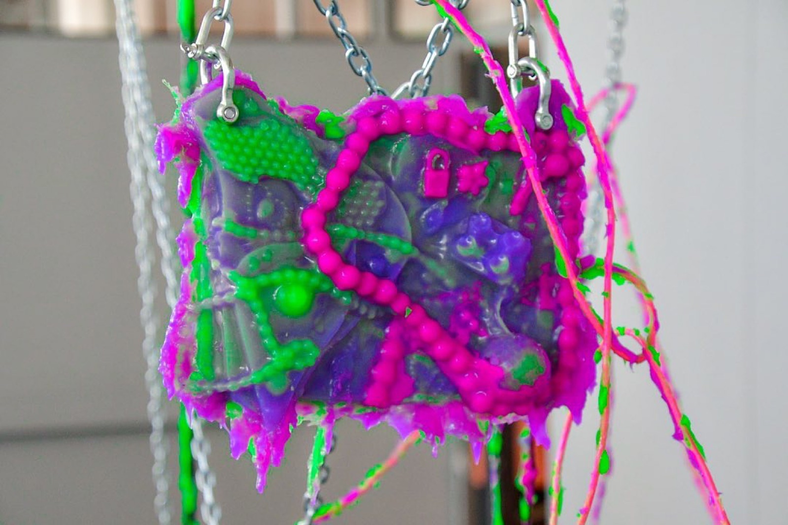 close up of a small panel entirely coated in bumpy purple and green cyberslime, a hot pink beaded chain crossed over it in an x, a tiny padlock charm and star beads pressed into the surface.